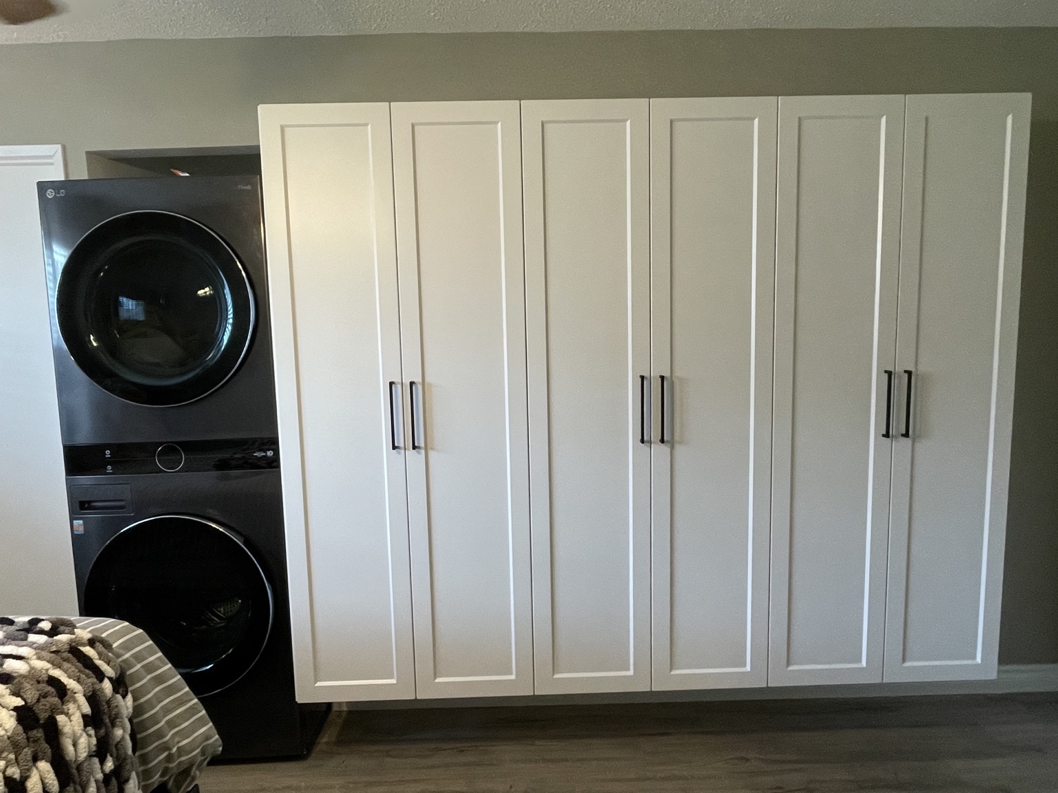 Six tall white shaker cabinet doors with black handles beside a stacked washer and dryer